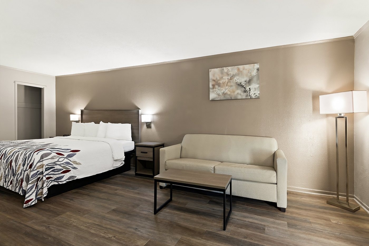 King standard room at Red Roof Inn Monroe — dark hardwood floors, warm lighting, sitting chair