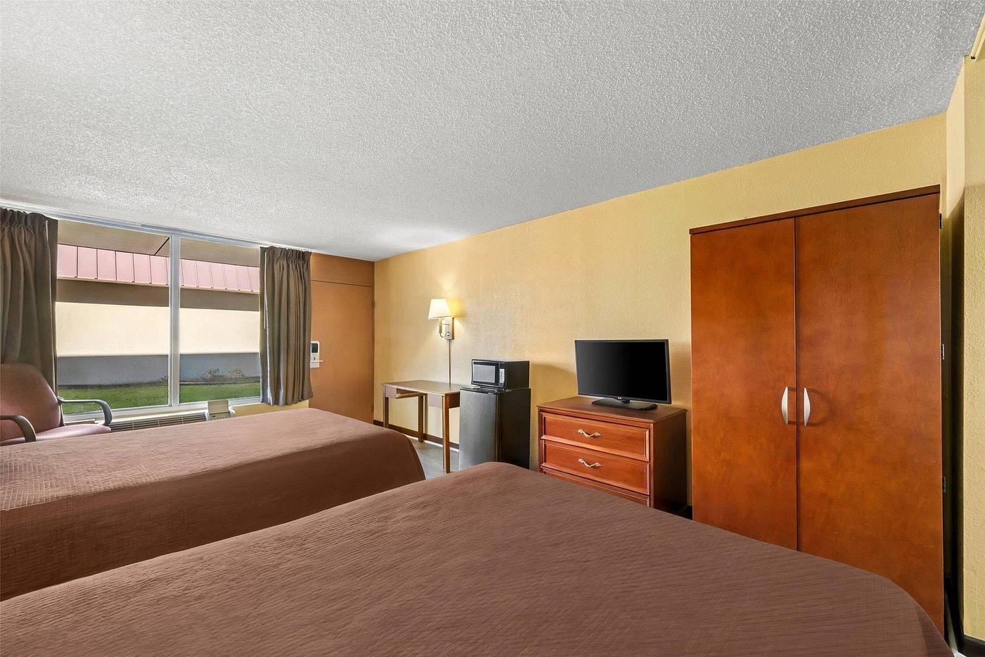 King room at Rodeway Inn Monroe — orange accent wall, wood headboard, wall sconces, bathroom visible