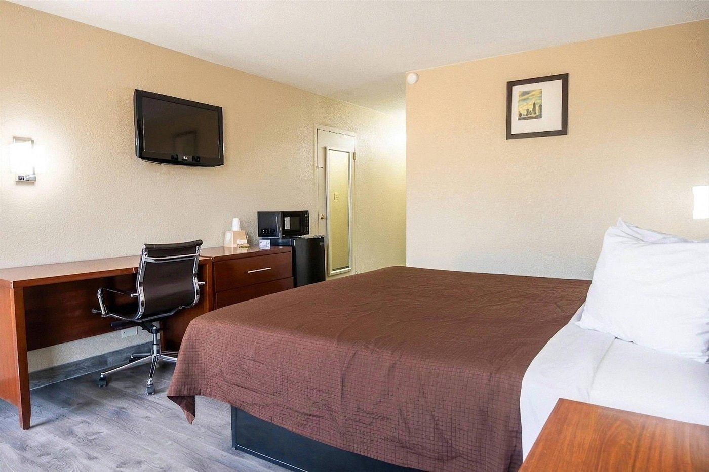 King room at Rodeway Inn Monroe — yellow walls, wood armoire, TV on dresser, microwave, work desk with red chair